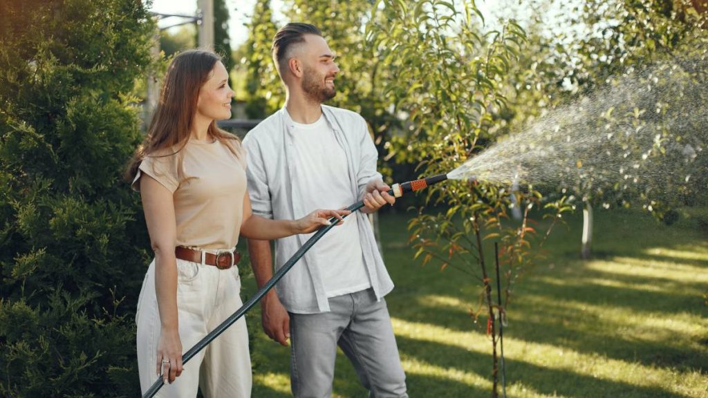 Couple watering garden with hosepipe
