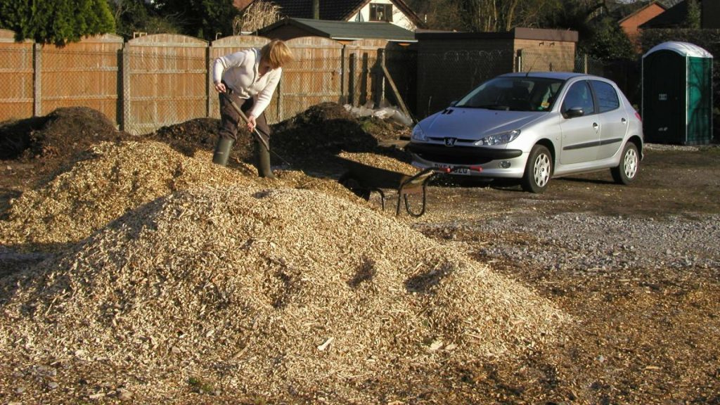 Lady standing on pile of woodchips with shovel